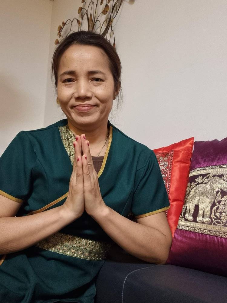 Masseurin in traditioneller thailändischer Kleidung begrüßt Gäste mit einem Wai